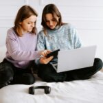 two-girls-sitting-on-a-bed-looking-at-a-laptop