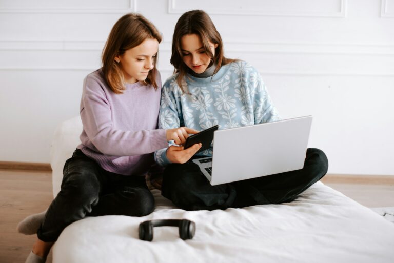 two-girls-sitting-on-a-bed-looking-at-a-laptop