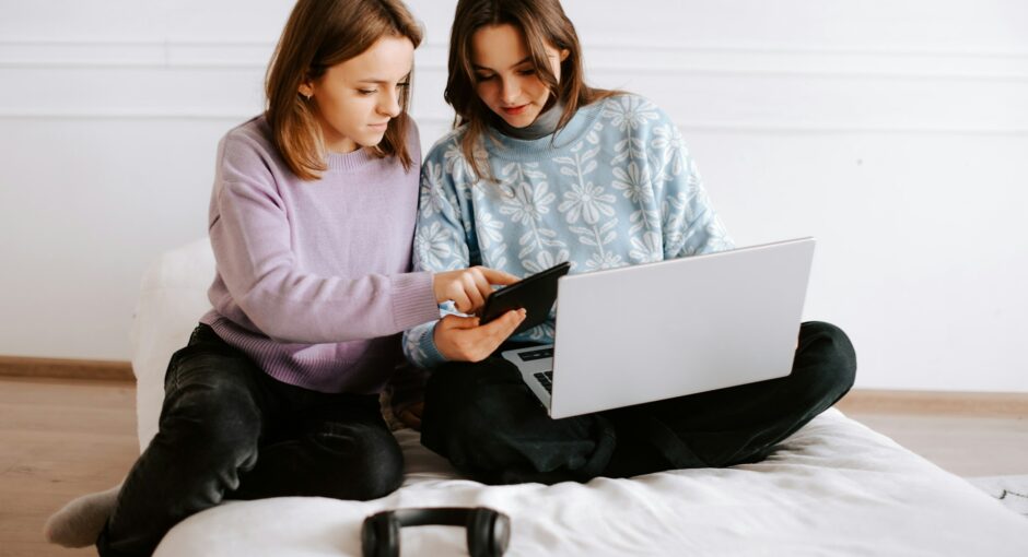 two-girls-sitting-on-a-bed-looking-at-a-laptop
